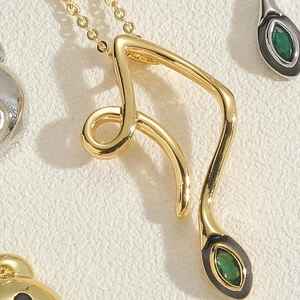 Close-up of golden streamlined pendant necklace with a green gemstone and enamel detail