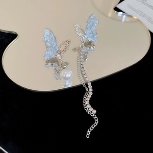 Détail de boucles d'oreilles papillon bleu avec perle et chaîne à pompon en strass
