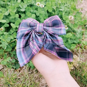 Close-up of a plaid bow hair clip in blue, purple, and pink fabric held outdoors
