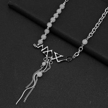 Detail of silver geometric pendant with white beads and metallic fringe on dark surface