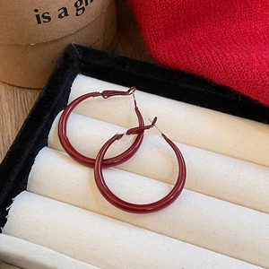 Macro detail of wine red enamel hoop earrings on beige velvet jewelry display