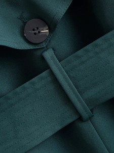Detail of dark green trench coat showing twill fabric texture and four-hole button