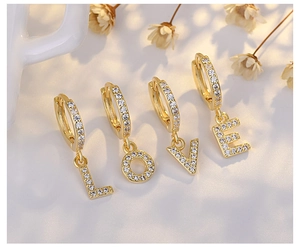 Detail of four gold S925 silver hoop earrings spelling LOVE with sparkling zircon stones