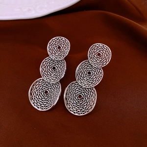 Close-up of silver triple-layered hollow geometric mesh drop earrings on red velvet