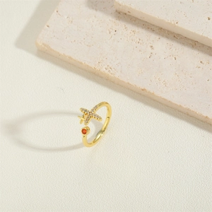 Golden open ring featuring a crystal airplane design and a red round gemstone accent