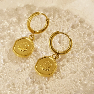 Golden hoop earrings with octopus relief charms on a shimmering ocean-style background