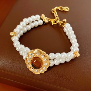 Dettaglio bracciale a due strati di perle con fiore dorato e pietra occhio di tigre