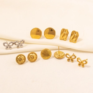 Flat lay of gold and silver bow and geometric stud earrings on white silk fabric