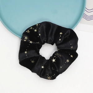 Detail of a black velvet hair scrunchie with metallic gold star patterns and soft texture
