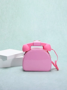 Creative pink telephone shaped crossbody bag with handset handle on white pedestal
