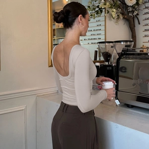 Elegante top beige a maniche lunghe con schiena scoperta e scollo a U in un caffè raffinato