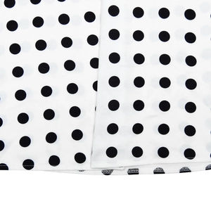 Vue détaillée du tissu en satin blanc à pois noirs avec une bordure d'ourlet soignée