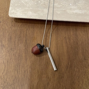 Close-up of wooden acorn pendant with silver metal tube on long necklace chain