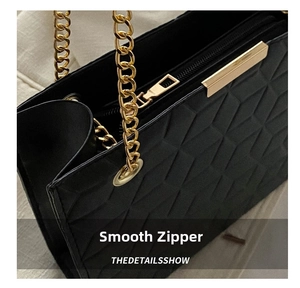 Detail of smooth gold zipper and geometric texture on black leather tote bag