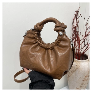Macro detail of brown pleated dumpling bag showing knotted handle and soft leather texture