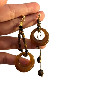 Hand holding vintage asymmetric tiger eye stone and resin hoop drop earrings with gold chain