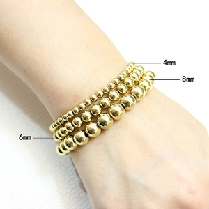 Detail view of 4mm, 6mm, and 8mm gold beaded bracelets shown on a model's wrist