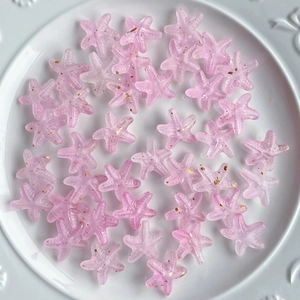 Macro shot of pink gradient acrylic starfish beads with gold glitter in a white bowl