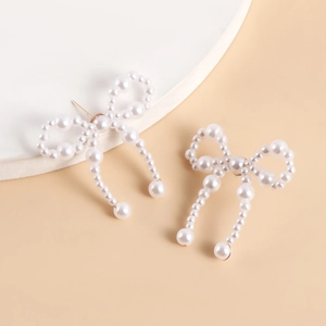 Detailed view of handmade bow-shaped earrings featuring polished white pearls and metal studs
