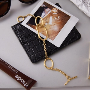Macro detail of golden OT clasp bracelet on a textured black surface with stylish accessories