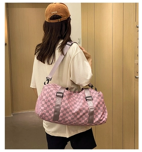 Model carrying pink checkered duffel bag for travel over shoulder in indoor setting