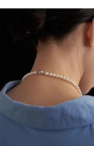 Detail of elegant pearl necklace with metal clasp on model neck against blue shirt background