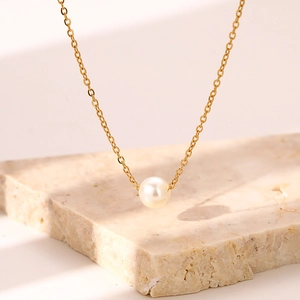 Elegant gold chain necklace with a round pearl pendant on a marble background