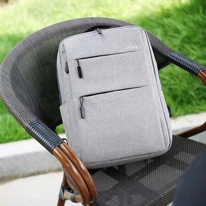 Light gray business backpack with USB port on a rattan chair in outdoor lawn setting