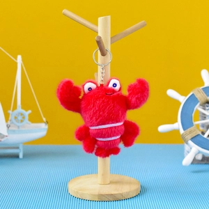 Close-up of a cute red plush crab keychain hanging on a wooden display stand