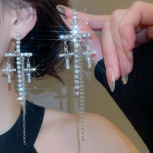 Detail shot of silver dangling cross earrings with sparkling rhinestones and chain tassels