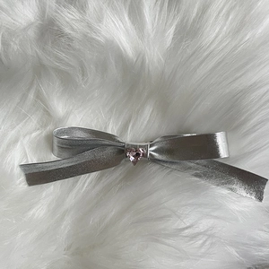 Detail of silver bow hair clip with pink heart rhinestone on white faux fur background