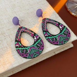 Gros plan de boucles d'oreilles bohèmes avec clous violets et motifs peints sur un carnet