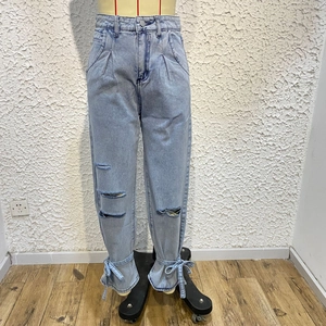 Detail view of light blue denim jeans with distressed holes and ankle tie-up design