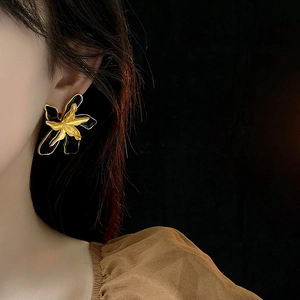 Close-up of vintage flower earrings in black and gold worn by a model in artistic light