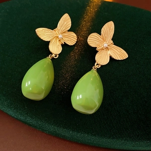 Détail de boucles d'oreilles papillon dorées avec perle et pendentif goutte en résine verte