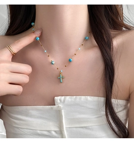 Close-up of bohemian gold necklace with blue enamel cross pendant on a female model