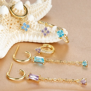 Detailed macro shot of gold geometric earrings with blue and purple zircons on satin