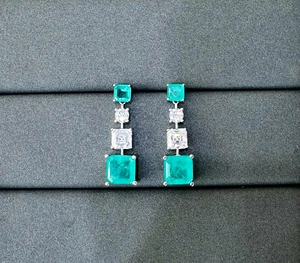Macro detail of silver earrings featuring stacked emerald green and clear square gemstones
