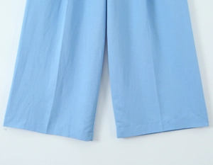 Detail of sky blue wide-leg trousers with vertical pleats and textured fabric