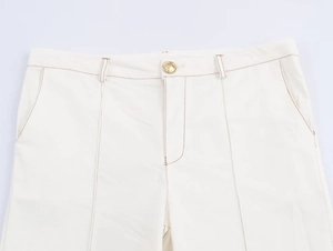 Detail of white high-waist trousers featuring golden button and brown contrast stitching