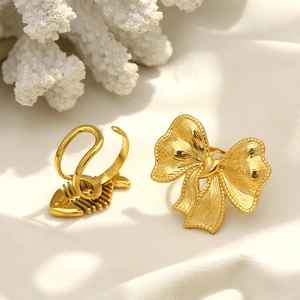 Detail view of 18K gold-plated stainless steel fishbone and bow rings on white fabric