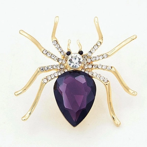 Detailed view of golden spider brooch with purple crystal and clear rhinestones