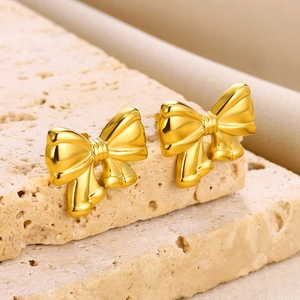 Detailed view of polished 18K gold bow-shaped earrings on a travertine background