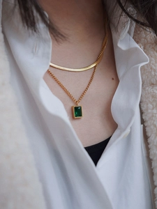 Detail of layered gold snake chain necklace with emerald green gemstone pendant on model