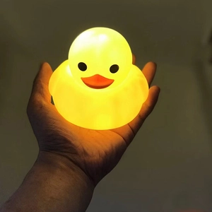 Close-up of a mini glowing yellow duck night light held in hand with warm light effect