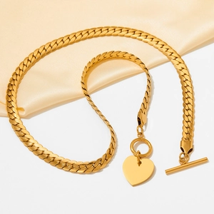 Detail view of gold Cuban chain necklace with heart pendant and T-bar clasp on silk cloth