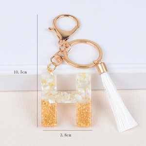 Detail view of resin letter H keychain with shell stones, gold foil, and white tassel