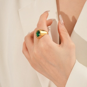 Dettaglio di un anello dorato vintage con gemma verde ovale indossato con classe