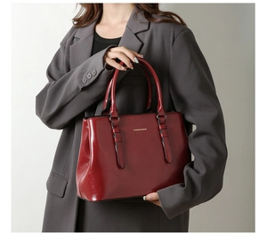 Detail of burgundy glossy tote bag held by model wearing a dark grey blazer jacket