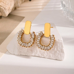 Close-up of gold C-shaped earrings with trapezoid zircon stones on white stone base